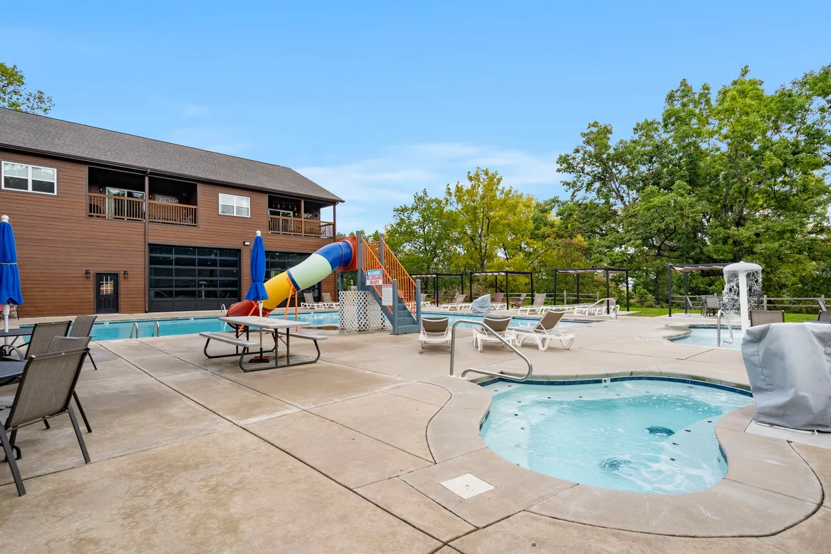 This exterior image captures the resort's swimming pool area, complete with a winding water slide, hot tub, and plenty of lounge chairs nestled amid lush trees. The space is lively and inviting, perfect for both active play and relaxing in the sun.