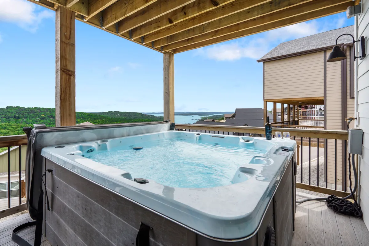A serene exterior view featuring a hot tub overlooking a scenic landscape, framed by wooden structures. The scene suggests relaxation and unwinding, with views likely extending toward the lake or natural surroundings.