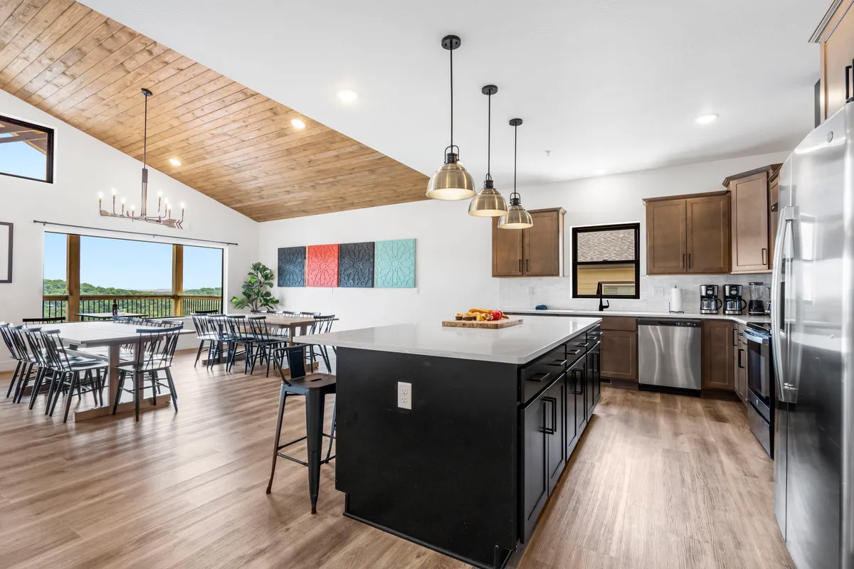 This interior shot captures a large kitchen island, adjacent dining table, colorful wall art, and panoramic windows. The space is bathed in natural light, emphasizing roominess and comfort for group gatherings.