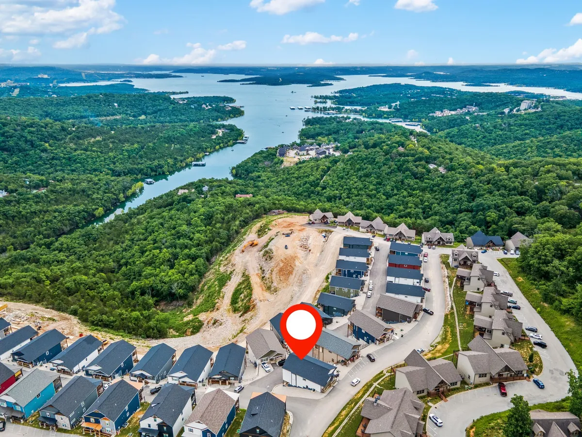 A serene lakeside view with homes visible on the opposite shore and greenery all around, suggesting easy access to outdoor adventures like boating, hiking, and nature walks. The tranquil atmosphere highlights the proximity to the lake.