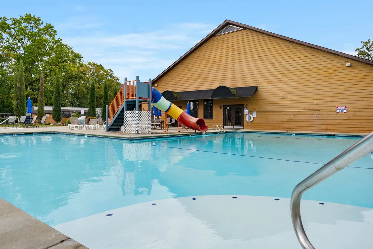 This vibrant exterior image shows a lively swimming pool area equipped with a water slide, colorful play structure, and plenty of lounge chairs, capturing the playful resort-style atmosphere. The scene radiates energy as children enjoy the slide and families relax nearby, perfectly matching the promise of group recreation and all-ages fun.