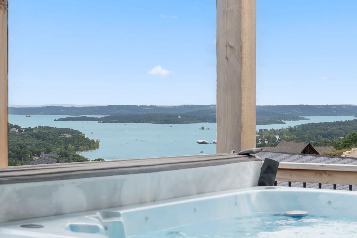 An exterior scene showing a private hot tub overlooking the shimmering lake, perfectly positioned for relaxation. The tranquil mood is amplified by the serene water view and the sense of seclusion, making it the perfect spot to unwind after energetic gaming sessions inside.