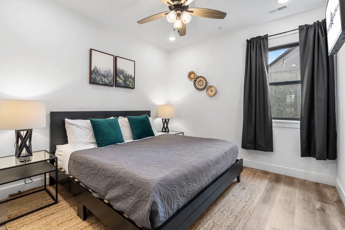 This image features a calm and restful bedroom with a bed dressed in luxurious, textured bedding, nightstands with lamps, wall art, and flowing curtains. The room is bathed in soft natural light, creating a peaceful sanctuary perfect for relaxation and sleep.