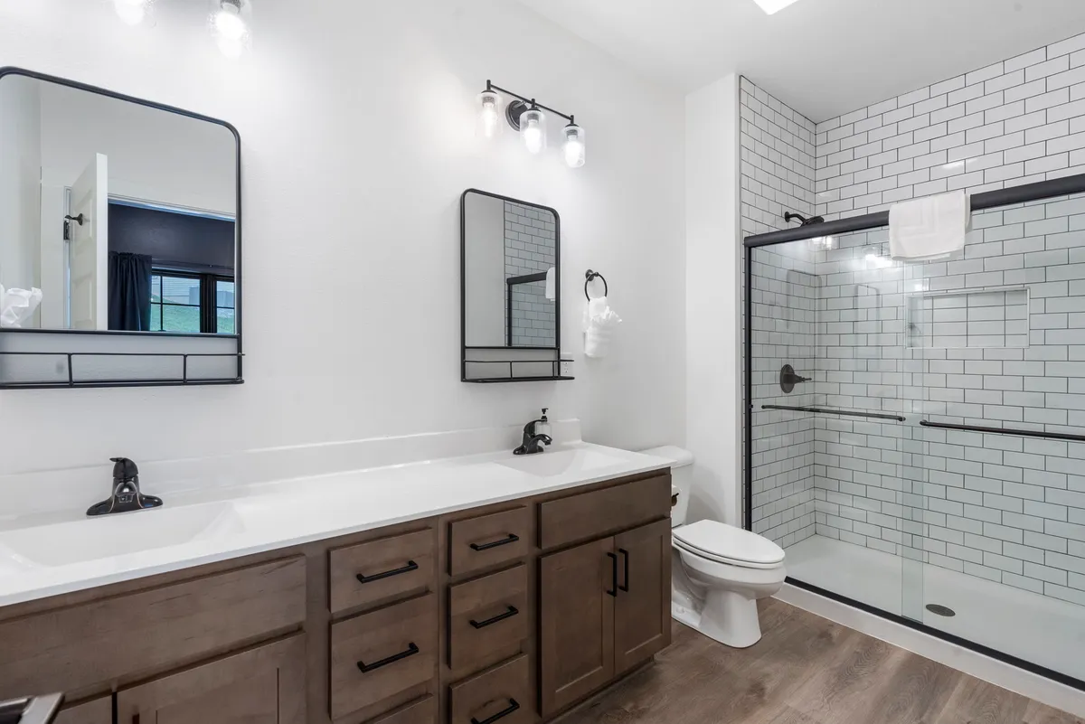 A luxurious ensuite bathroom featuring a double sink vanity, large mirrors, and a glass-enclosed shower. The space is filled with light, clean lines, and elegant finishes, offering a spa-like environment.