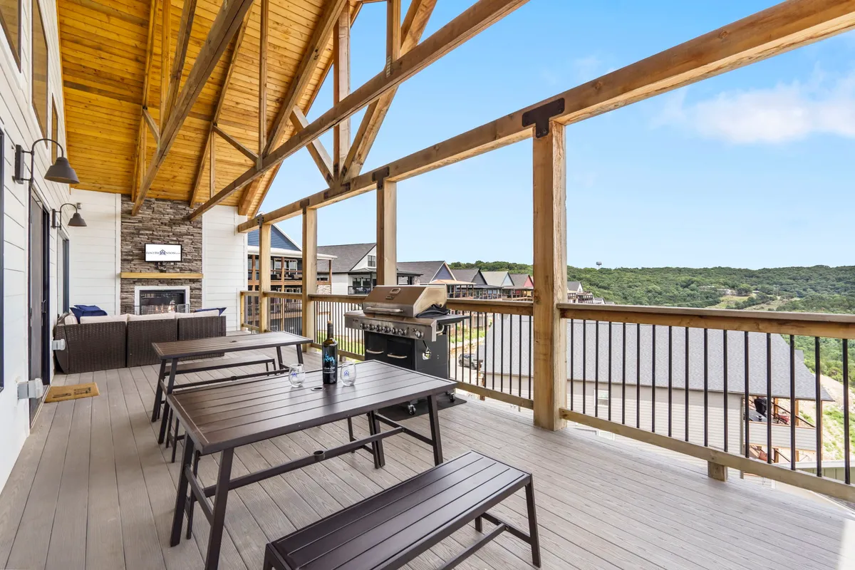 An exterior view of a covered outdoor dining area with a barbecue grill, wooden beams, and a scenic backdrop. The space is designed for relaxation and group gatherings, showcasing opportunities for outdoor meals and celebrations, especially in milder seasons like spring and fall.