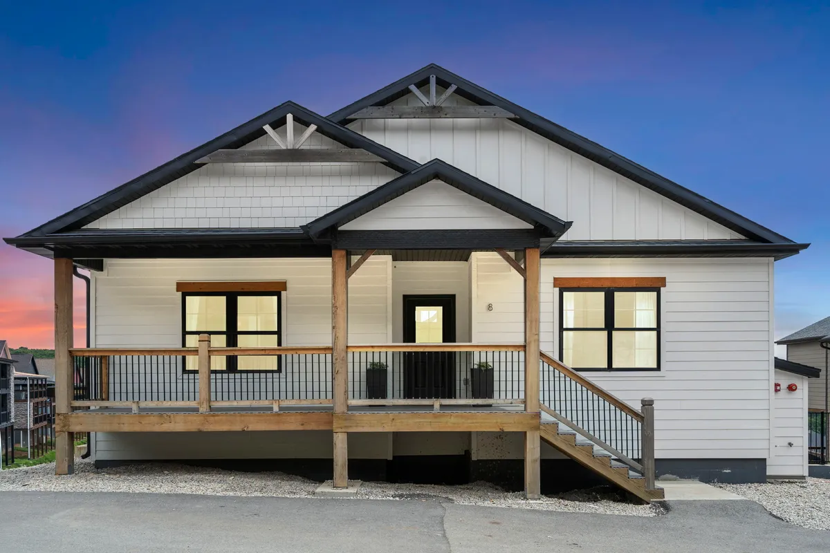 A welcoming front porch with symmetrical rooflines, wooden railings, and large windows overlooking manicured landscaping. The porch is spacious, inviting, and perfectly positioned for sunset views or outdoor gatherings.