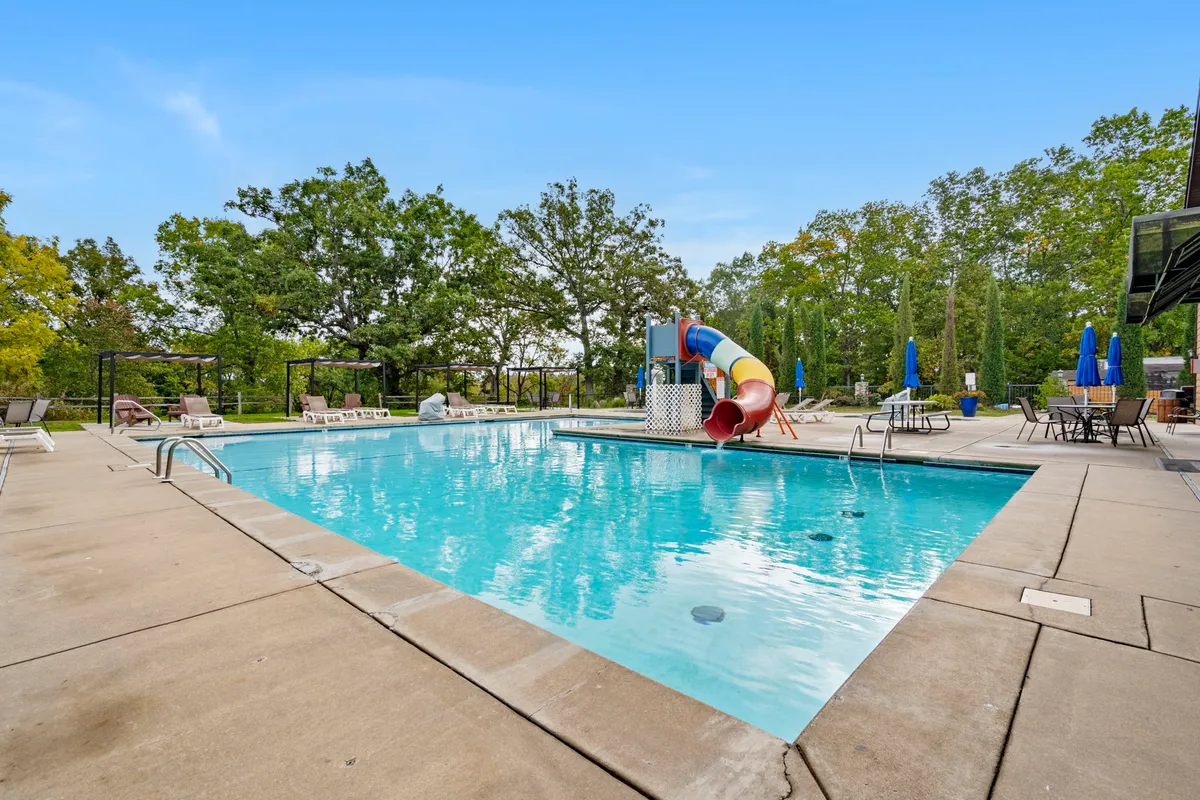 A vibrant exterior scene of the resort’s outdoor swimming pool, featuring an inviting water slide, lounge chairs, and blue umbrellas. The pool area is bathed in sunlight, with families and guests able to enjoy swimming, sunbathing, and gathering together for summertime fun.