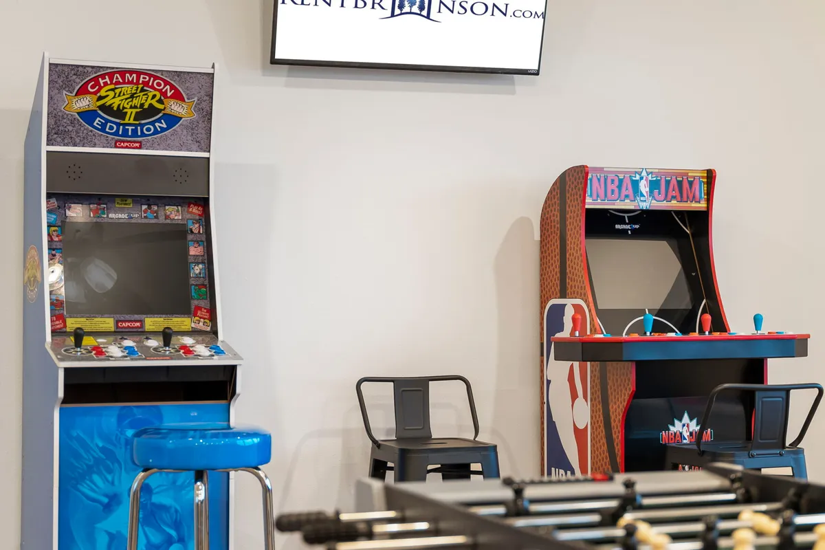 A close-up of the classic arcade games and a foosball table, with vibrant stool seating stationed nearby. The room's casual, nostalgic vibe invites playful competition and shared laughter, evoking the spirit of friendly rivalry. The arrangement suggests an intimate, interactive setting ideal for spirited gaming and group bonding.