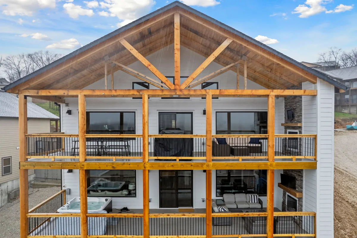 An expansive wooden deck featuring a hot tub, large windows, and wooden beams, with stunning views of the surrounding landscape. The scene is set for outdoor relaxation and memorable moments with family or friends.