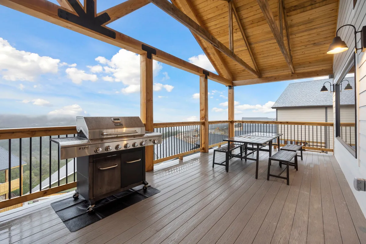 An inviting outdoor patio features a grill, picnic table, exposed wooden beams, and a beautiful mountain view. The space is designed for gathering, enjoying meals outdoors, and taking in the natural surroundings, combining private enjoyment with communal experiences.