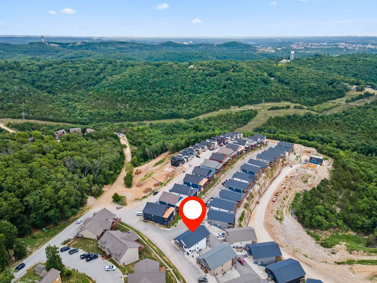 A wide exterior view of newly constructed resort homes surrounded by lush greenery and a gently curved road. The scene suggests peaceful nature walks, community gatherings, and seasonal changes, with hints of autumn foliage and open spaces for family outings.